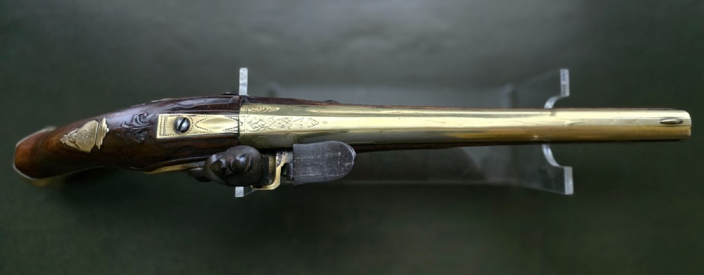 An 18th-century French flintlock holster pistol featuring a carved walnut stock, polished brass barrel, engraved brass lockplate, and steel mechanism. View XXIV
