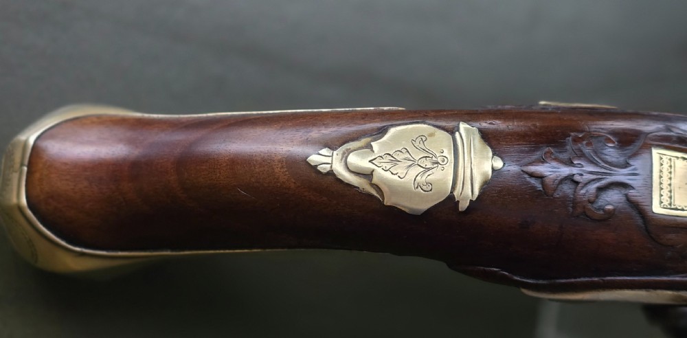 An 18th-century French flintlock holster pistol featuring a carved walnut stock, polished brass barrel, engraved brass lockplate, and steel mechanism. View XXVI