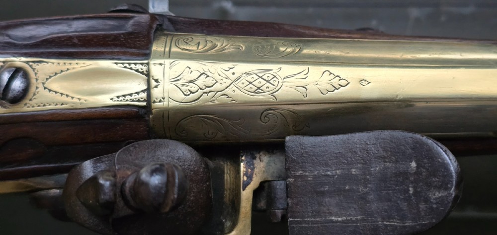 An 18th-century French flintlock holster pistol featuring a carved walnut stock, polished brass barrel, engraved brass lockplate, and steel mechanism. View XXVII