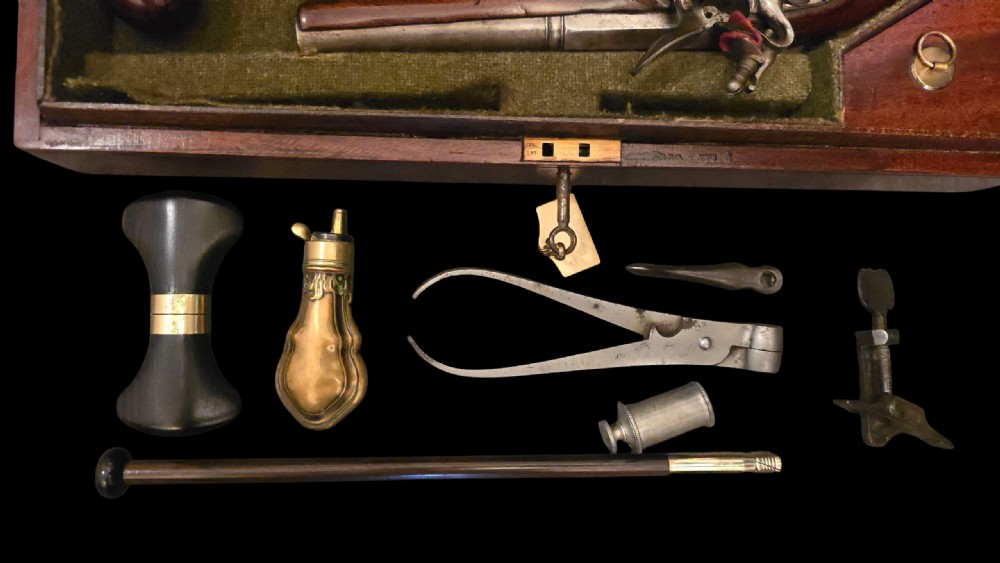 A fitted mahogany wooden case lined with green baize containing a pair of flintlock duelling pistols, a ramrod, and loading accessories. View II