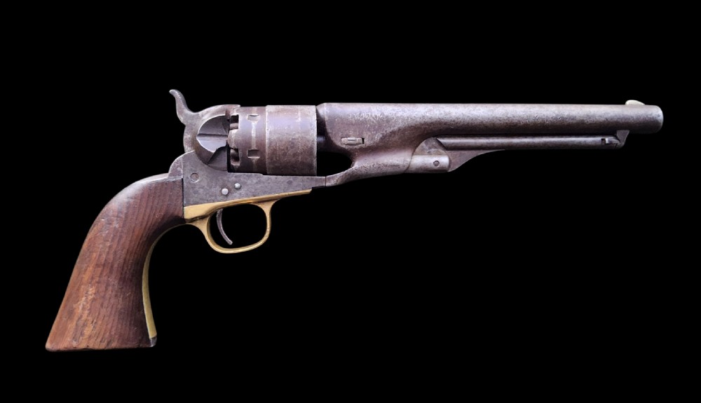 Side profile of a patinated steel Colt Model 1860 Army percussion revolver featuring a walnut handle grip and brass trigger guard.