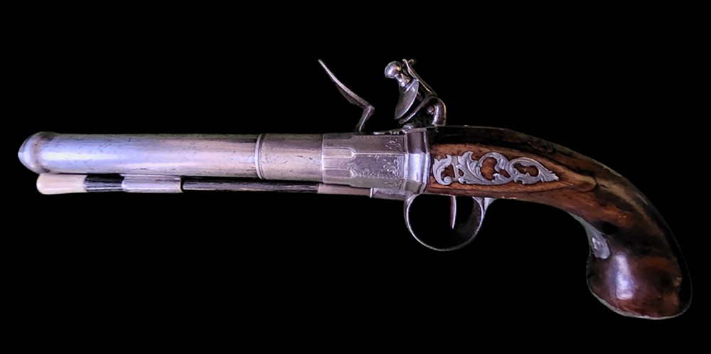 A mid-18th century flintlock pistol featuring a figured walnut stock, steel mechanism, and engraved silver mounts. View IV