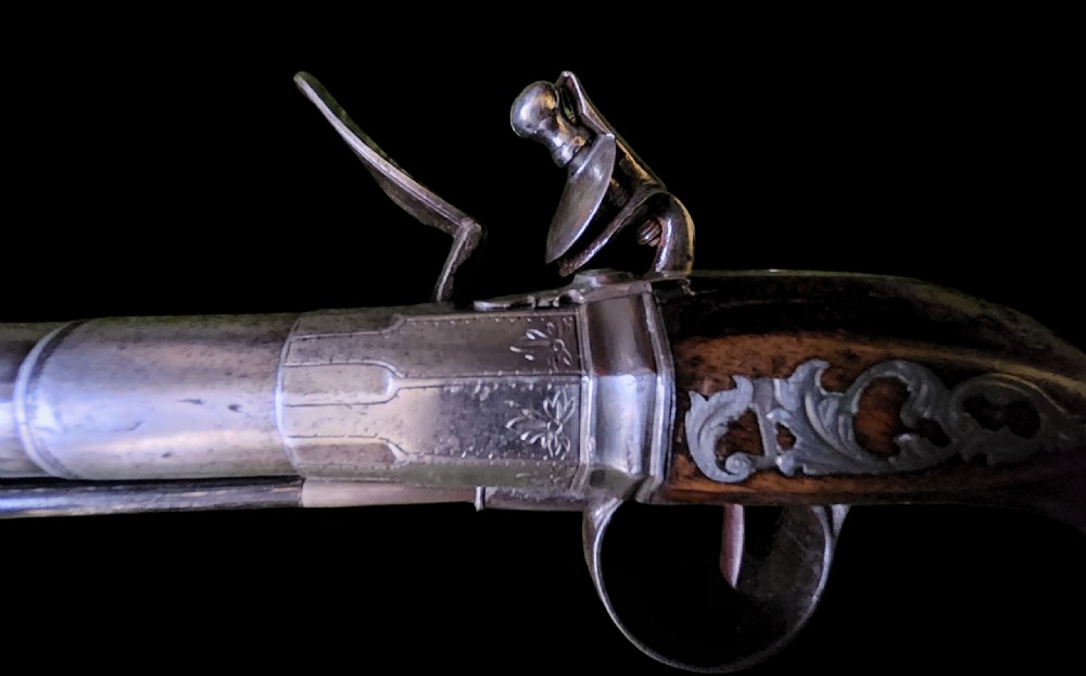 A mid-18th century flintlock pistol featuring a figured walnut stock, steel mechanism, and engraved silver mounts. View VII