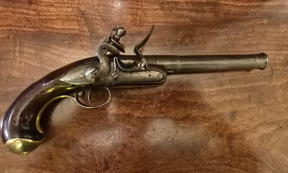 An 18th-century English Queen Anne flintlock turn-off pistol featuring an engraved steel mechanism, round steel barrel, dark walnut stock, and a brass butt cap. View IX