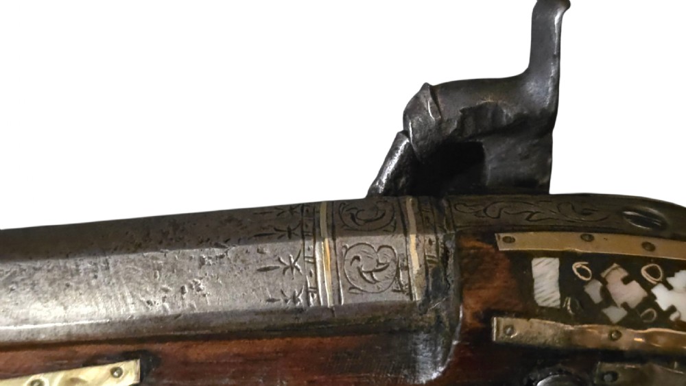 A 19th-century Ottoman pistol featuring a dark wood stock inlaid with mother-of-pearl geometric designs and brass wire, with an engraved steel mechanism and barrel. View XIV