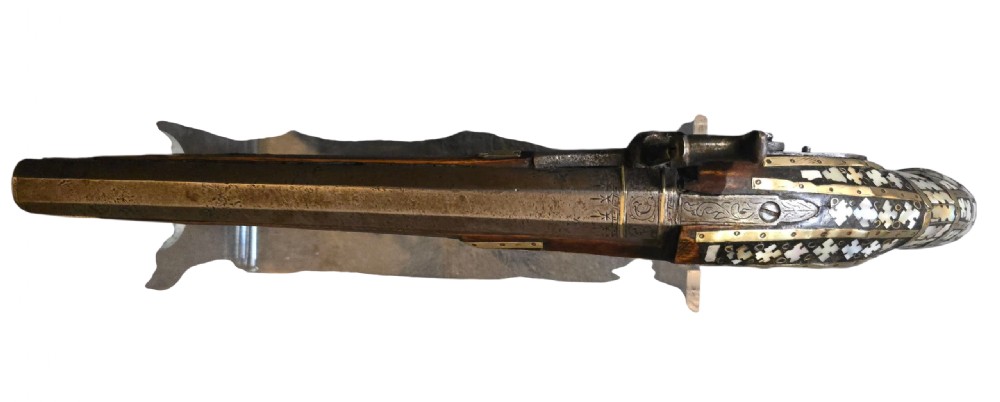 A 19th-century Ottoman pistol featuring a dark wood stock inlaid with mother-of-pearl geometric designs and brass wire, with an engraved steel mechanism and barrel. View XVI