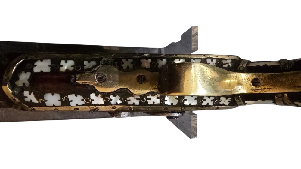 A 19th-century Ottoman pistol featuring a dark wood stock inlaid with mother-of-pearl geometric designs and brass wire, with an engraved steel mechanism and barrel. View XX