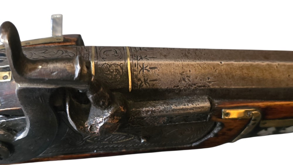 A 19th-century Ottoman pistol featuring a dark wood stock inlaid with mother-of-pearl geometric designs and brass wire, with an engraved steel mechanism and barrel. View XXI