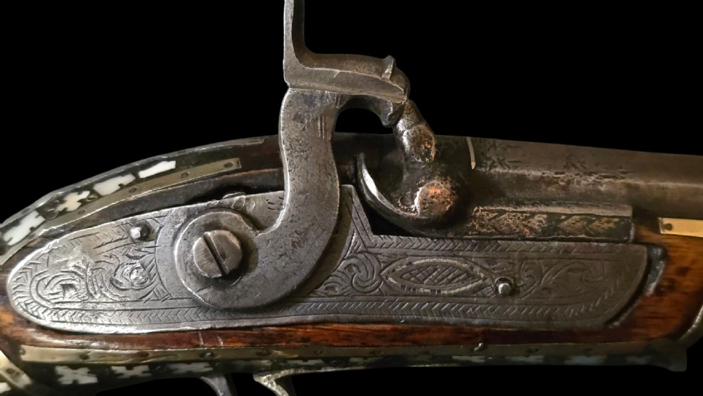 A 19th-century Ottoman pistol featuring a dark wood stock inlaid with mother-of-pearl geometric designs and brass wire, with an engraved steel mechanism and barrel. View XXVI