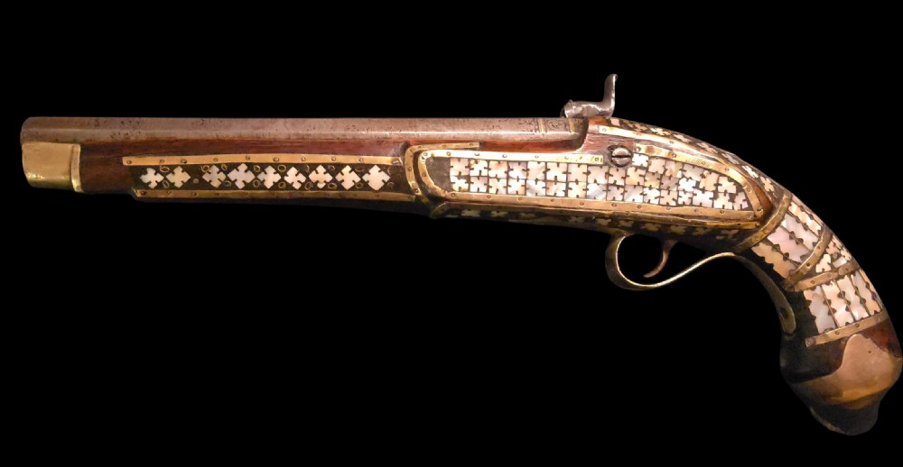 A 19th-century Ottoman pistol featuring a dark wood stock inlaid with mother-of-pearl geometric designs and brass wire, with an engraved steel mechanism and barrel. View XXVIII