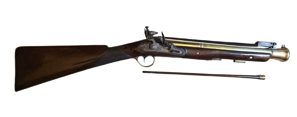 Late eighteenth-century British flintlock blunderbuss featuring a flared brass barrel, dark polished walnut stock, steel flintlock action, top-mounted sprung bayonet, and a separate wooden ramrod.