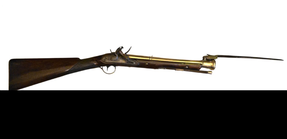 Late eighteenth-century British flintlock blunderbuss featuring a flared brass barrel, dark polished walnut stock, steel flintlock action, top-mounted sprung bayonet, and a separate wooden ramrod. View II