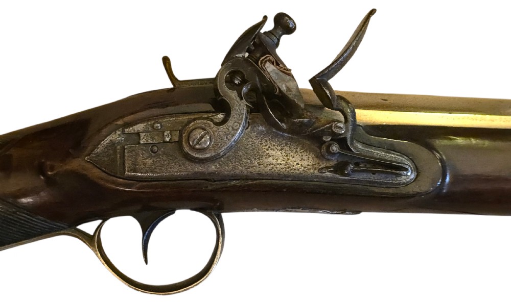 Late eighteenth-century British flintlock blunderbuss featuring a flared brass barrel, dark polished walnut stock, steel flintlock action, top-mounted sprung bayonet, and a separate wooden ramrod. View V