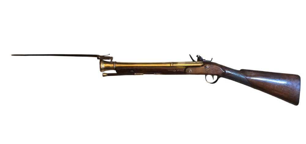 Late eighteenth-century British flintlock blunderbuss featuring a flared brass barrel, dark polished walnut stock, steel flintlock action, top-mounted sprung bayonet, and a separate wooden ramrod. View X