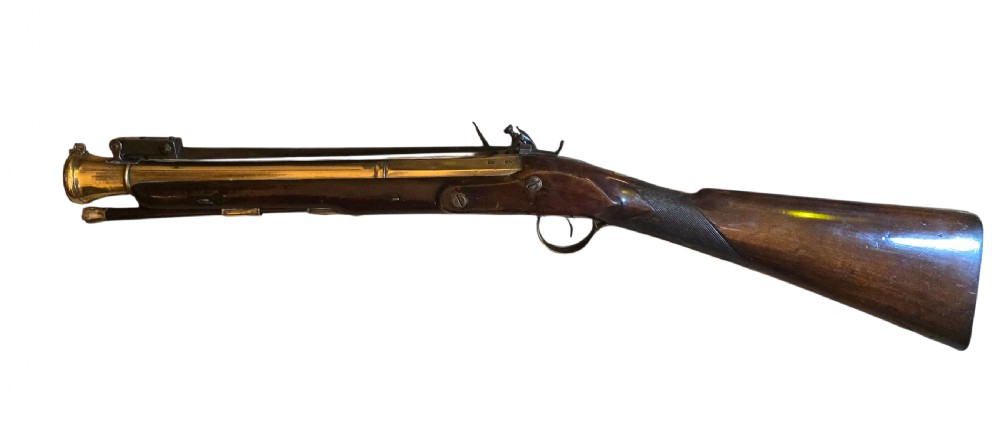 Late eighteenth-century British flintlock blunderbuss featuring a flared brass barrel, dark polished walnut stock, steel flintlock action, top-mounted sprung bayonet, and a separate wooden ramrod. View XVIII