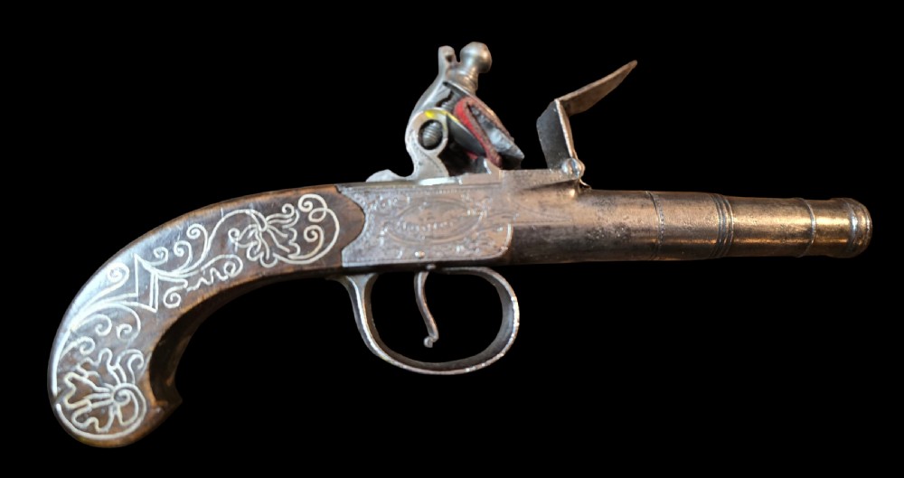 An 18th-century English flintlock pocket pistol featuring a steel cannon barrel, engraved action, and a dark wooden grip with inlaid silver wire scrollwork.