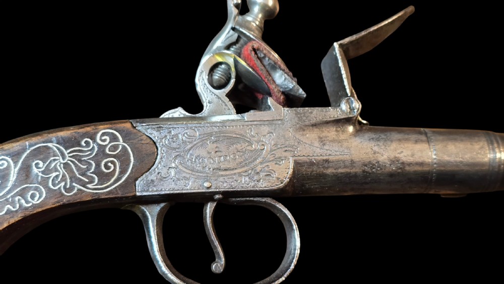 An 18th-century English flintlock pocket pistol featuring a steel cannon barrel, engraved action, and a dark wooden grip with inlaid silver wire scrollwork. View IV