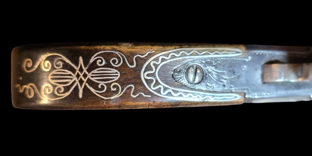 An 18th-century English flintlock pocket pistol featuring a steel cannon barrel, engraved action, and a dark wooden grip with inlaid silver wire scrollwork. View VII