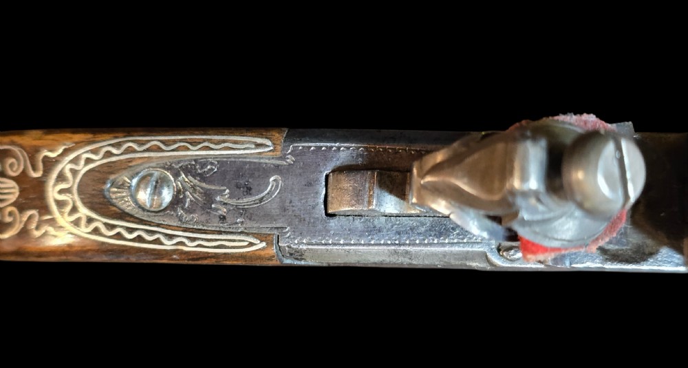 An 18th-century English flintlock pocket pistol featuring a steel cannon barrel, engraved action, and a dark wooden grip with inlaid silver wire scrollwork. View VIII