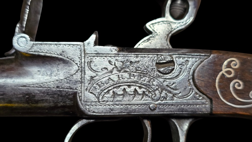 An 18th-century English flintlock pocket pistol featuring a steel cannon barrel, engraved action, and a dark wooden grip with inlaid silver wire scrollwork. View XIII
