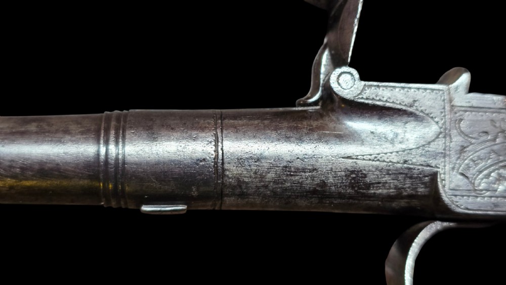 An 18th-century English flintlock pocket pistol featuring a steel cannon barrel, engraved action, and a dark wooden grip with inlaid silver wire scrollwork. View XIV