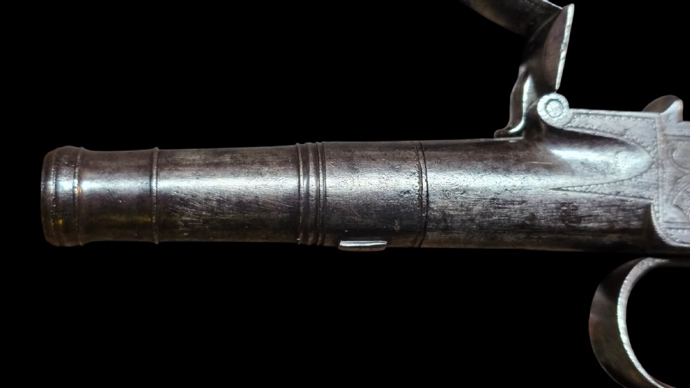 An 18th-century English flintlock pocket pistol featuring a steel cannon barrel, engraved action, and a dark wooden grip with inlaid silver wire scrollwork. View XV