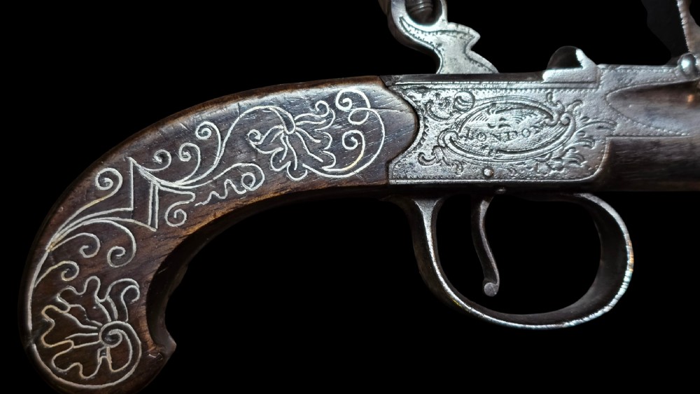 An 18th-century English flintlock pocket pistol featuring a steel cannon barrel, engraved action, and a dark wooden grip with inlaid silver wire scrollwork. View XXIII