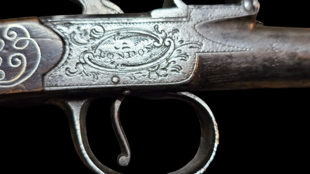 An 18th-century English flintlock pocket pistol featuring a steel cannon barrel, engraved action, and a dark wooden grip with inlaid silver wire scrollwork. View XXIV