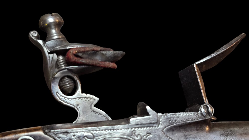 An 18th-century English flintlock pocket pistol featuring a steel cannon barrel, engraved action, and a dark wooden grip with inlaid silver wire scrollwork. View XXV