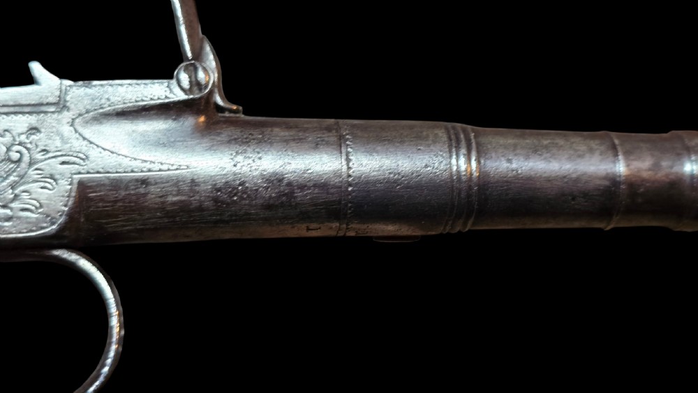 An 18th-century English flintlock pocket pistol featuring a steel cannon barrel, engraved action, and a dark wooden grip with inlaid silver wire scrollwork. View XXVI