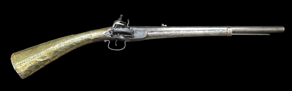 An eighteenth-century Ottoman Balkan flintlock musket carbine with a brass-sheathed stock featuring chased geometric patterns and a steel barrel.