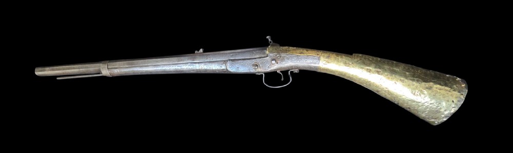 An eighteenth-century Ottoman Balkan flintlock musket carbine with a brass-sheathed stock featuring chased geometric patterns and a steel barrel. View IV