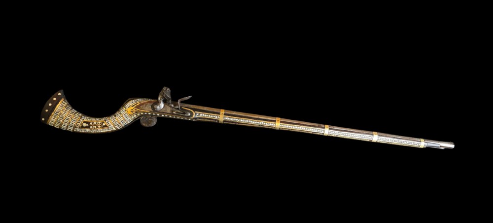 A late 18th-century Indo-Persian flintlock musket featuring a curved wooden stock inlaid with mother-of-pearl geometric patterns and bound with brass barrel bands.
