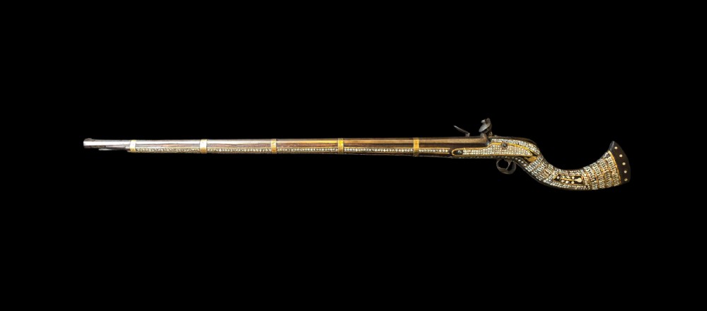 A late 18th-century Indo-Persian flintlock musket featuring a curved wooden stock inlaid with mother-of-pearl geometric patterns and bound with brass barrel bands. View VI