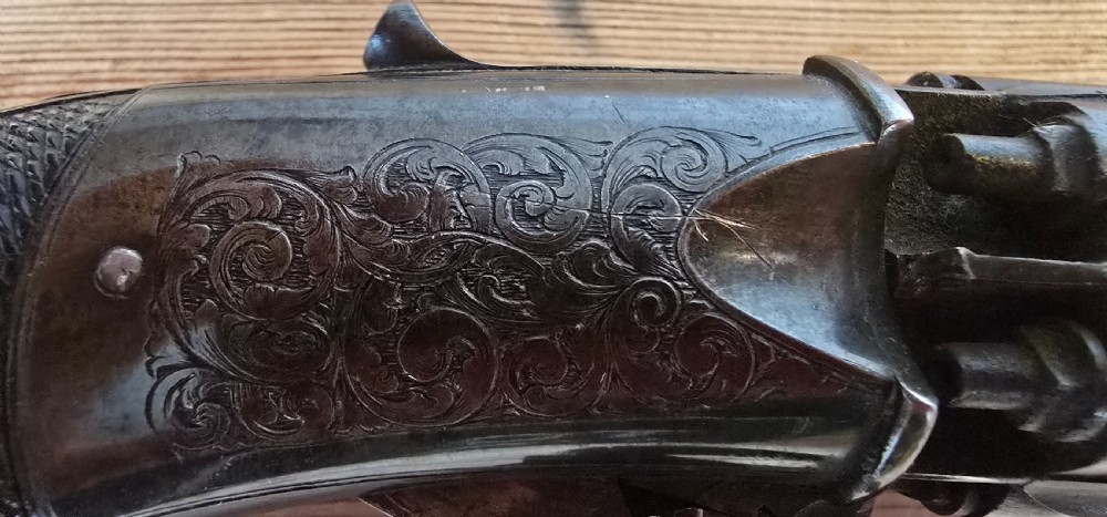 A nineteenth-century six-shot percussion pepperbox pistol featuring a multi-barrel steel cylinder, engraved frame, ring trigger, and chequered dark wood grip. View XVIII