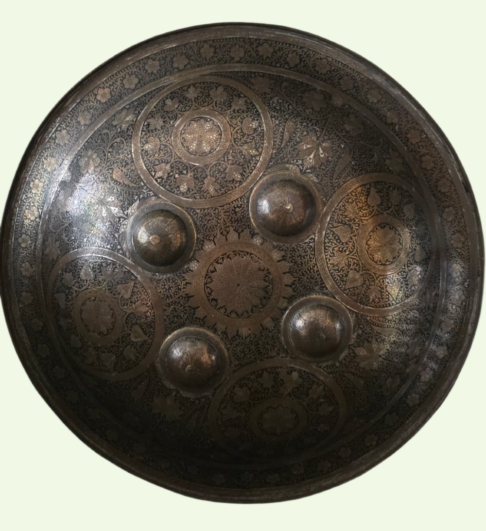 A circular late 19th-century Indian brass dhal shield featuring four central raised bosses and detailed engraved foliate patterns. View III
