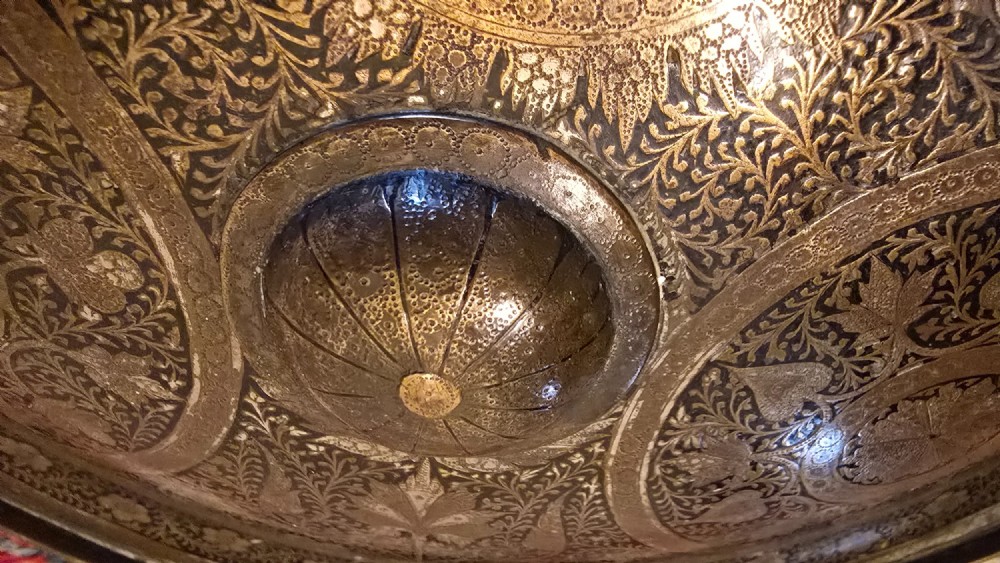 A circular late 19th-century Indian brass dhal shield featuring four central raised bosses and detailed engraved foliate patterns. View X