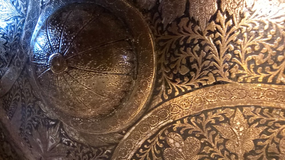 A circular late 19th-century Indian brass dhal shield featuring four central raised bosses and detailed engraved foliate patterns. View XI