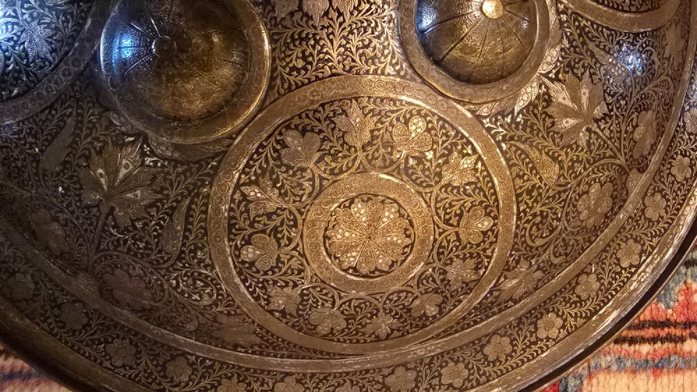 A circular late 19th-century Indian brass dhal shield featuring four central raised bosses and detailed engraved foliate patterns. View XII
