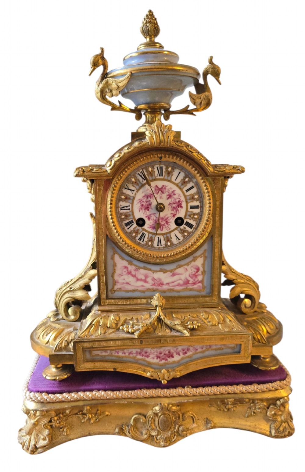 A French gilt bronze mantel clock decorated with hand-painted pink floral and cherub porcelain panels and topped with an urn flanked by swan handles.