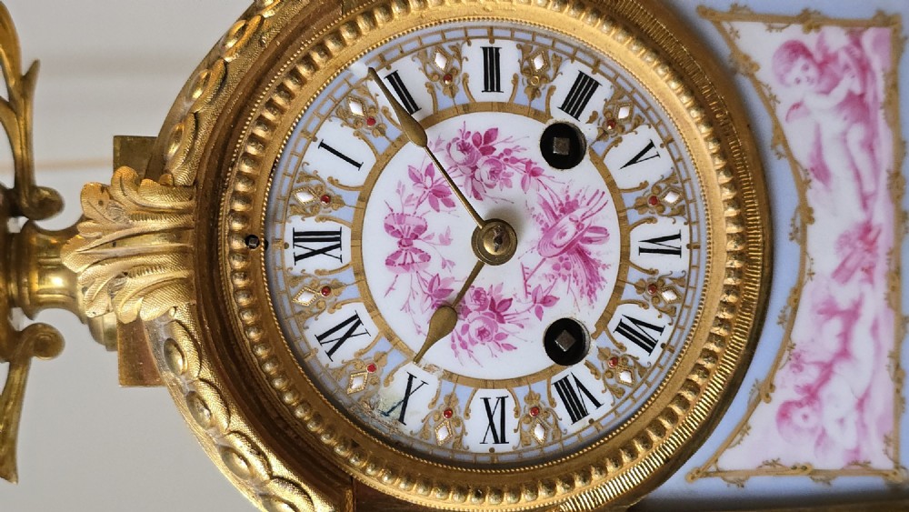 A French gilt bronze mantel clock decorated with hand-painted pink floral and cherub porcelain panels and topped with an urn flanked by swan handles. View IV