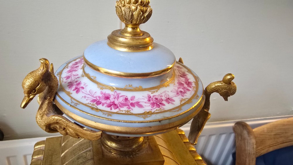 A French gilt bronze mantel clock decorated with hand-painted pink floral and cherub porcelain panels and topped with an urn flanked by swan handles. View IX