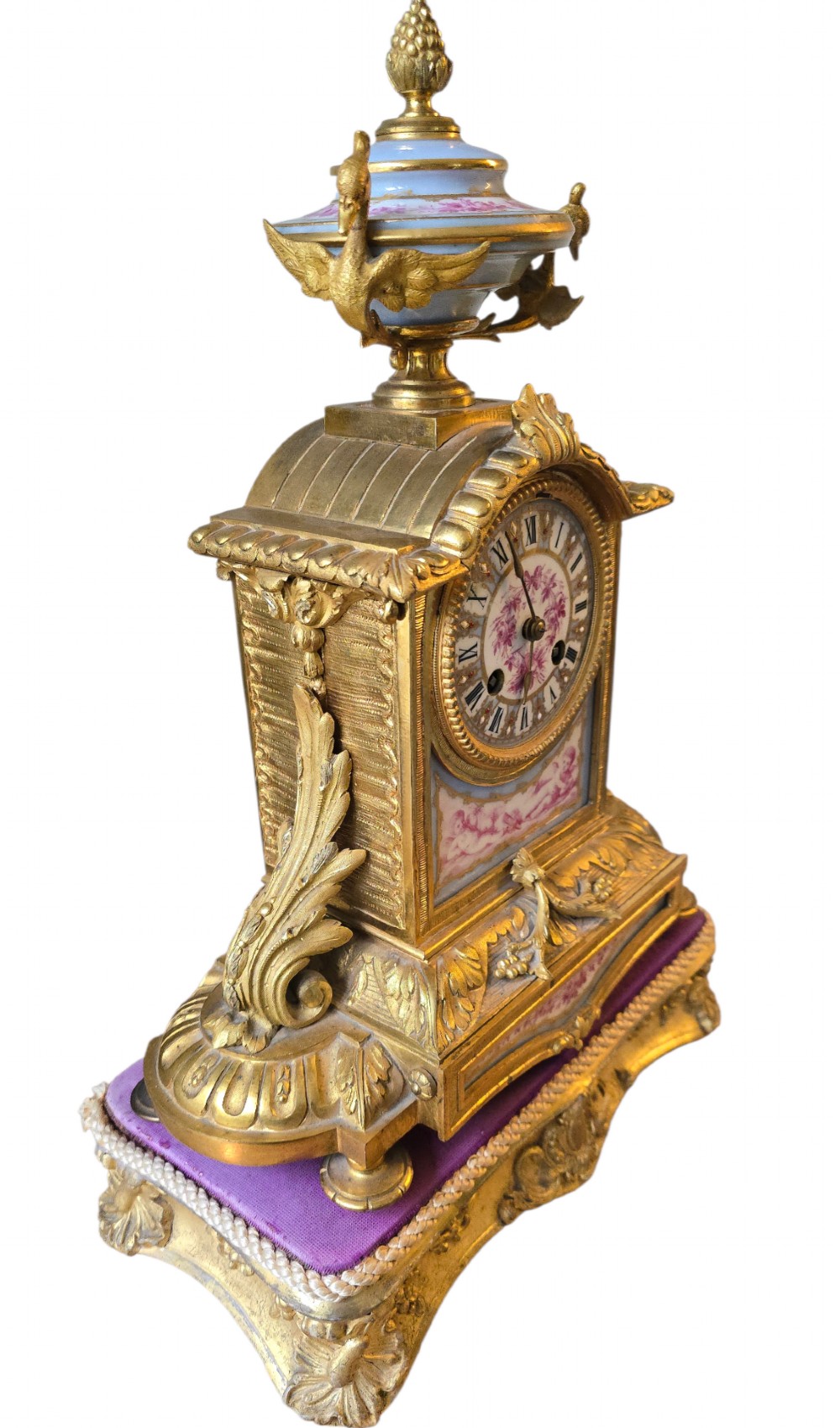 A French gilt bronze mantel clock decorated with hand-painted pink floral and cherub porcelain panels and topped with an urn flanked by swan handles. View X
