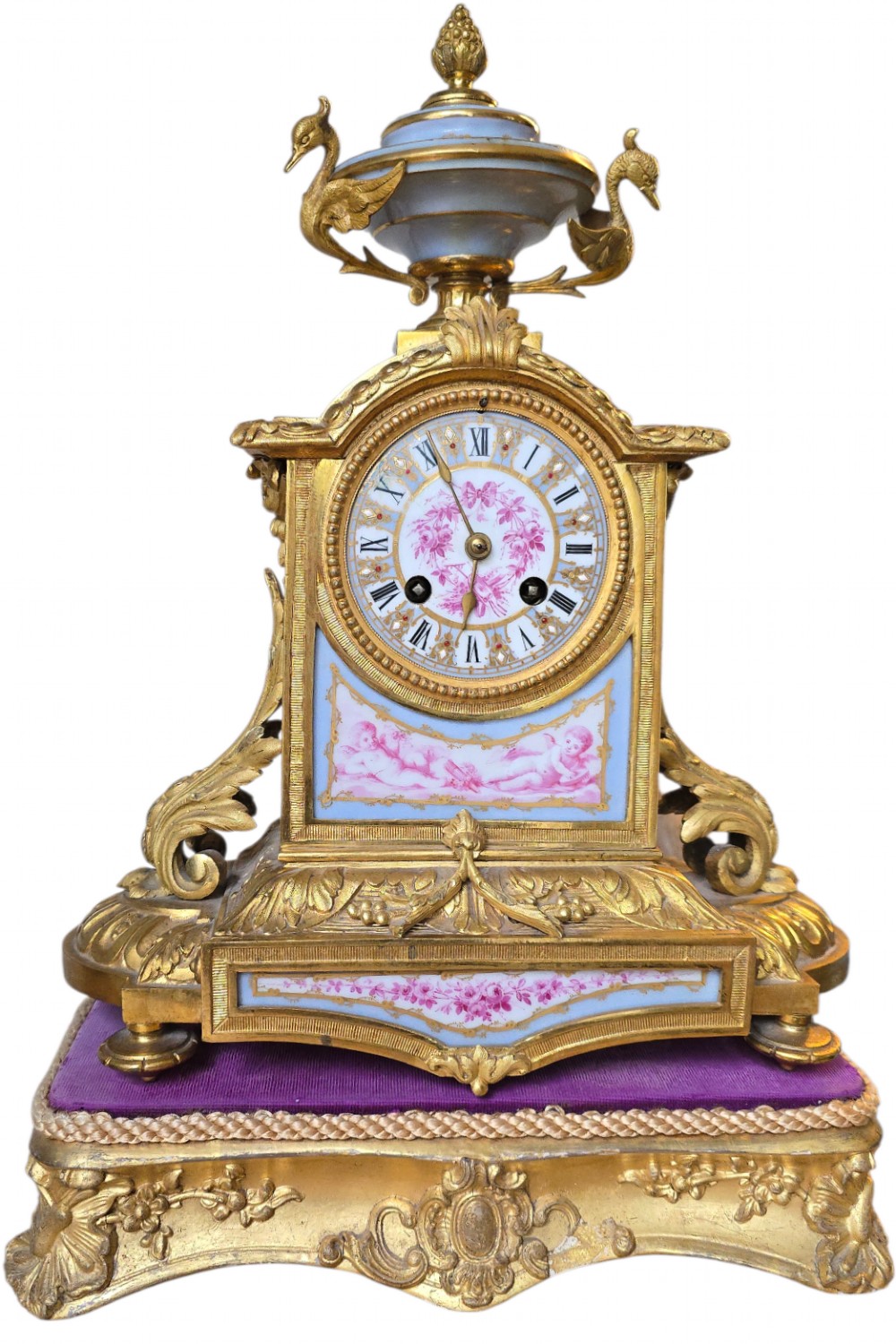 A French gilt bronze mantel clock decorated with hand-painted pink floral and cherub porcelain panels and topped with an urn flanked by swan handles. View XIV