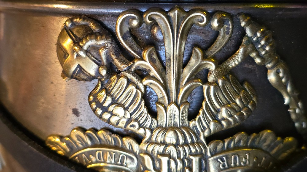 A WWI Prussian steel Pickelhaube helmet featuring a brass spiked top, a brass Prussian eagle emblem on the front, and a black strap. View X