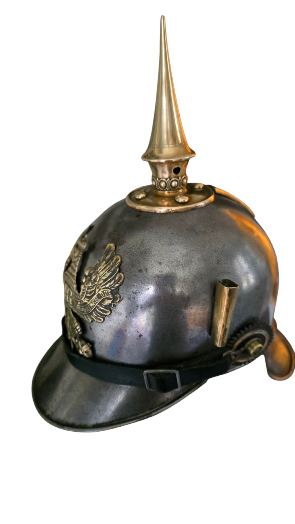 A WWI Prussian steel Pickelhaube helmet featuring a brass spiked top, a brass Prussian eagle emblem on the front, and a black strap. View XII