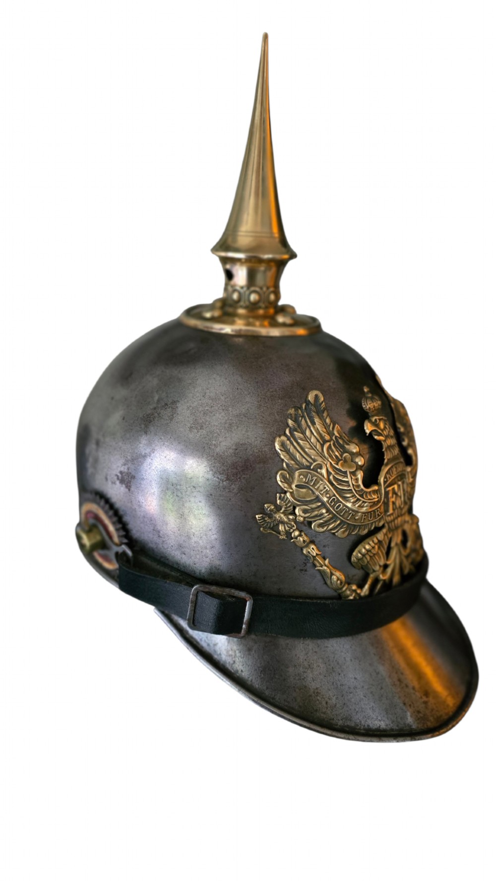 A WWI Prussian steel Pickelhaube helmet featuring a brass spiked top, a brass Prussian eagle emblem on the front, and a black strap. View XIII