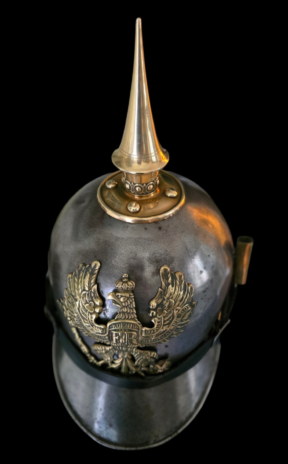 A WWI Prussian steel Pickelhaube helmet featuring a brass spiked top, a brass Prussian eagle emblem on the front, and a black strap. View XV