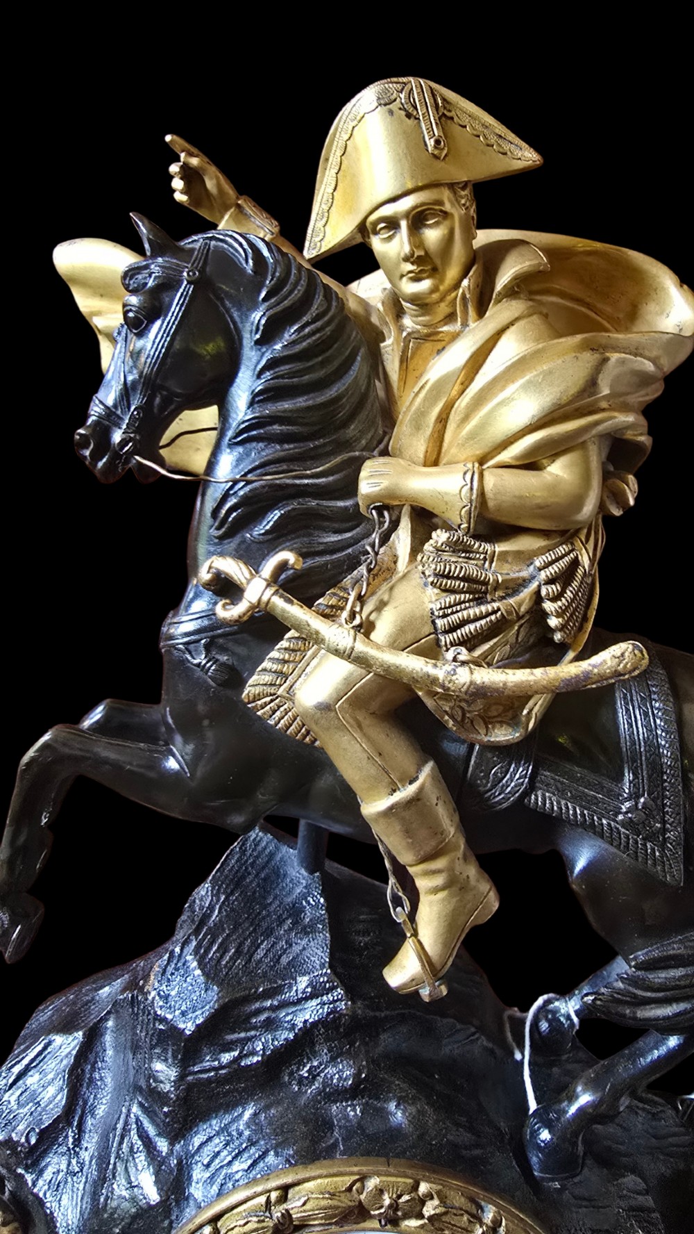 A 19th-century French mantel clock featuring a patinated and gilt bronze equestrian statue of Napoleon Bonaparte atop a base housing a white clock face with Roman numerals. View XII