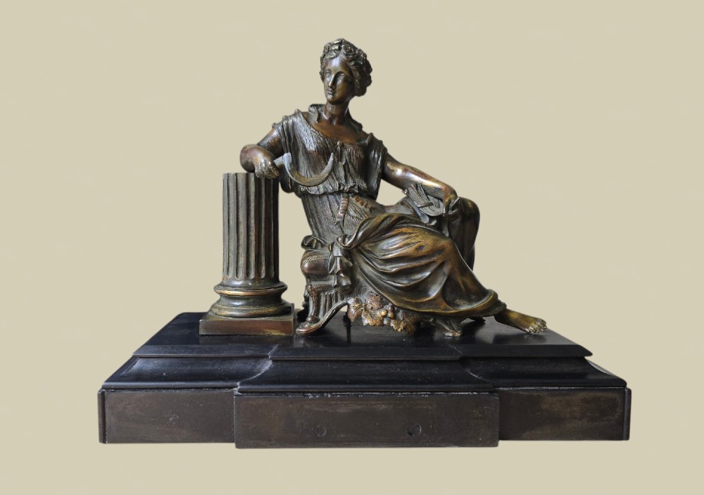 A 19th-century patinated bronze sculpture depicting the classical goddess Demeter seated beside a fluted column on a black stepped plinth.